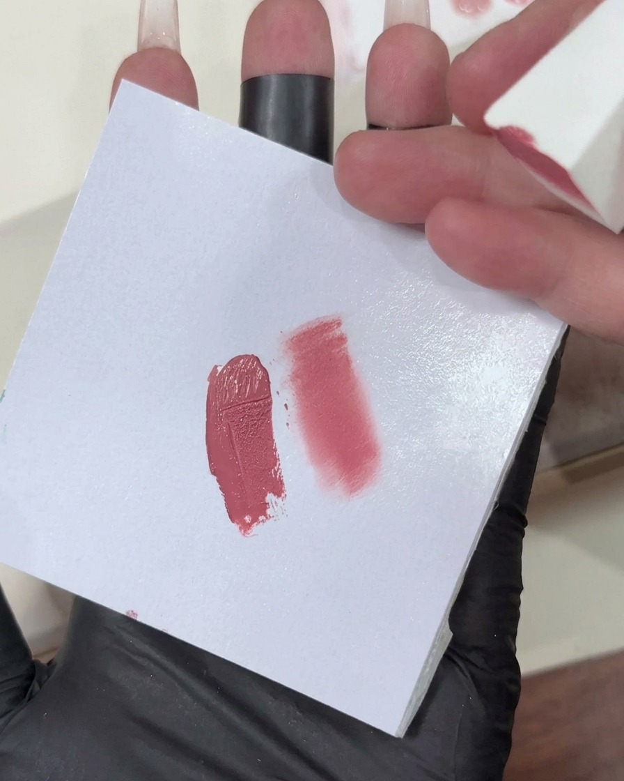 A makeup sponge with a light pink gel gradient being applied to the tip of a nail.