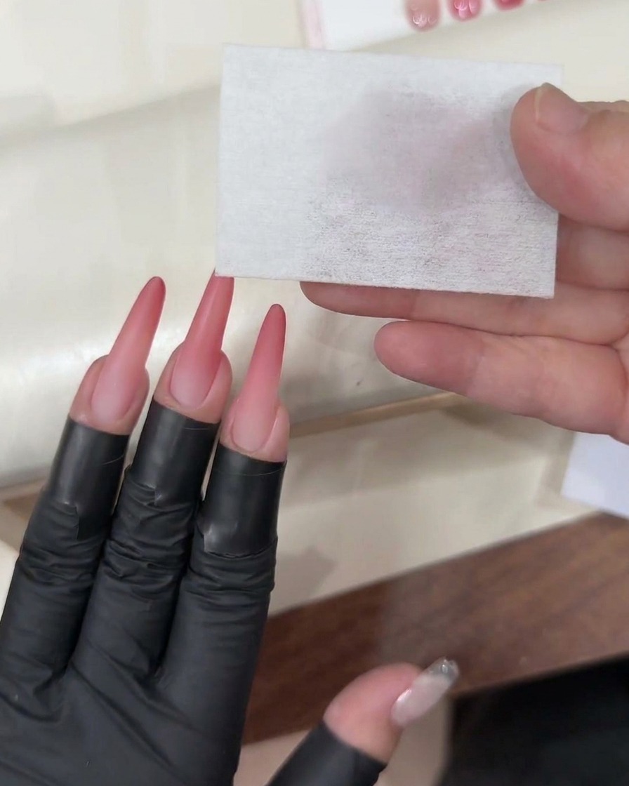 A gel brush applying a clear, glossy top coat over the finished pink ombré nail.