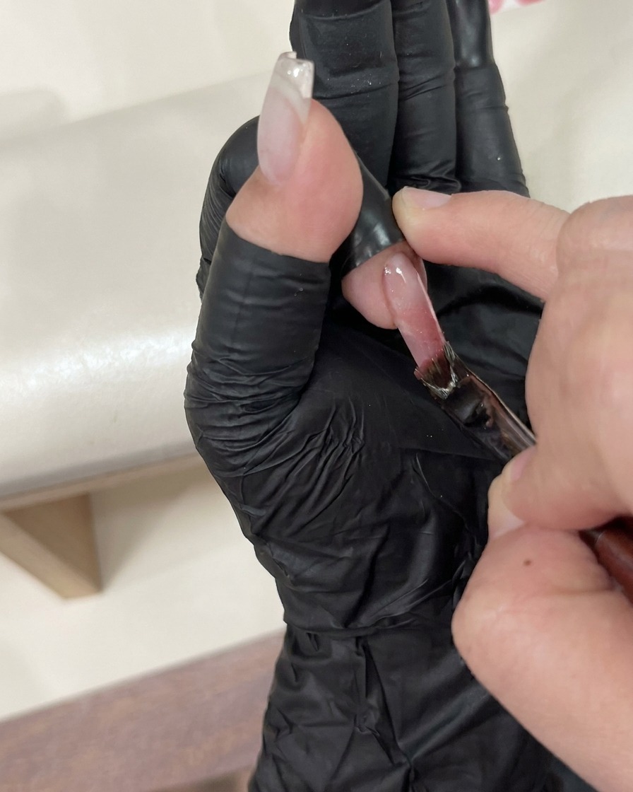 A pair of tweezers carefully placing a small decorative charm onto a wet top-coated nail.