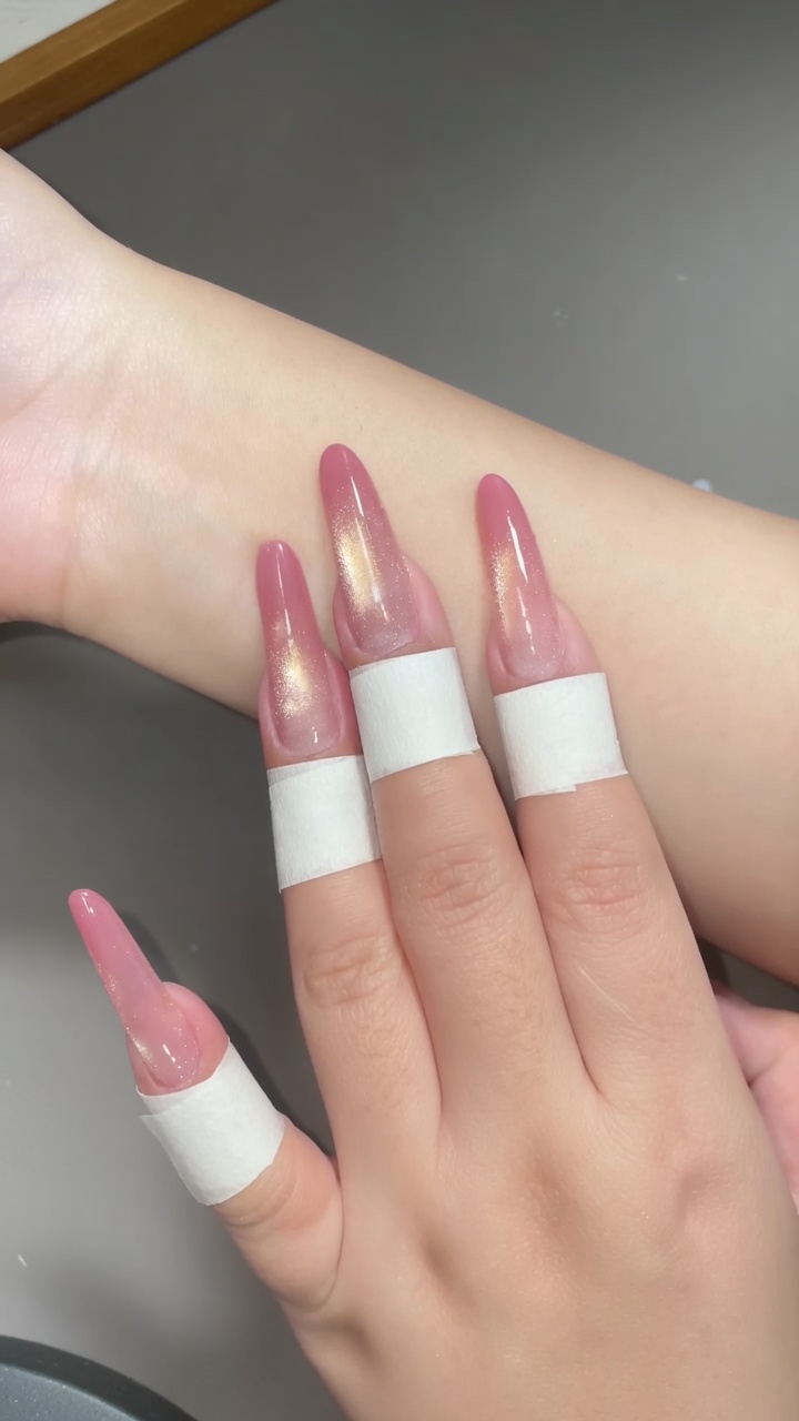 Stiletto-shaped clear extensions featuring a soft peach-pink gradient tip and a shimmering vertical gold cat-eye effect.