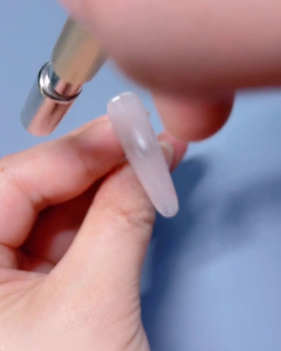 A magnetic tool being held near the wet gel-coated nail to manipulate the shimmer particles.
