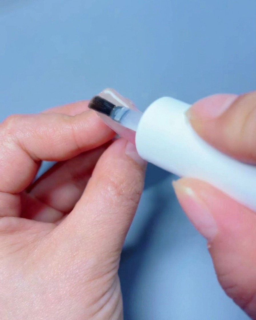 A hand positioned under a professional UV/LED nail lamp curing the final top coat.