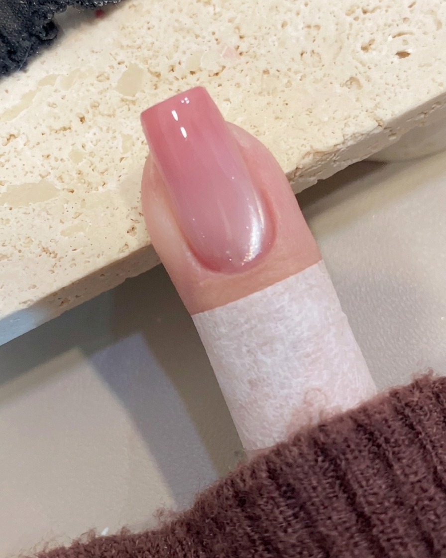 Close-up view of a hand carefully removing a piece of protective tape from the skin surrounding a manicured nail.