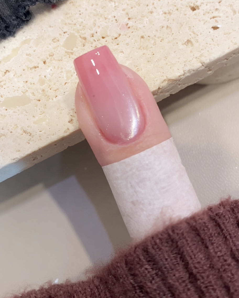 A close-up view showing a brush applying sheer shimmering cat-eye gel polish over a prepared nail.