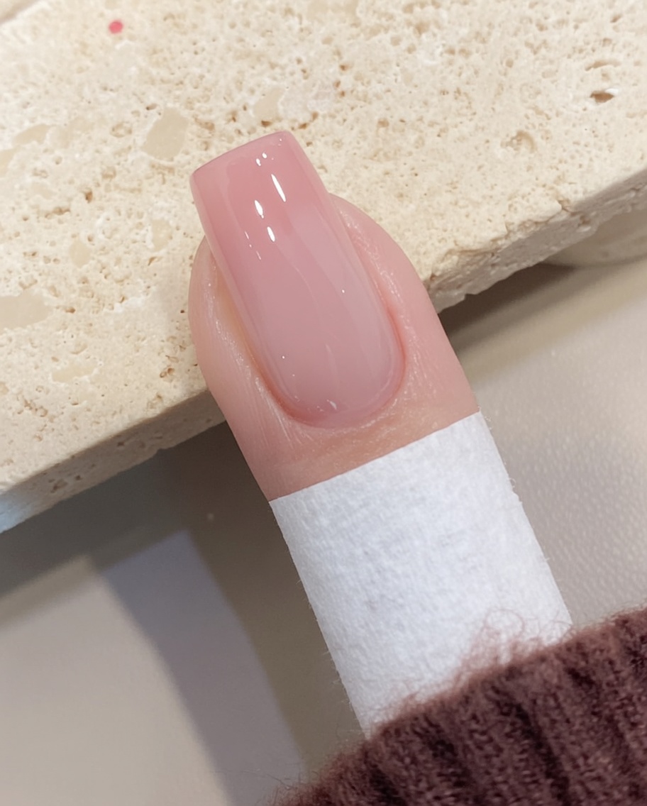 A lint-free wipe removing the tacky residue from a cured gel nail surface.