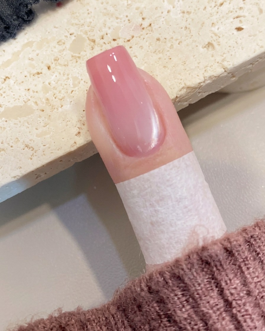 A small amount of peach-colored gel being placed at the free edge of the nail with a brush.