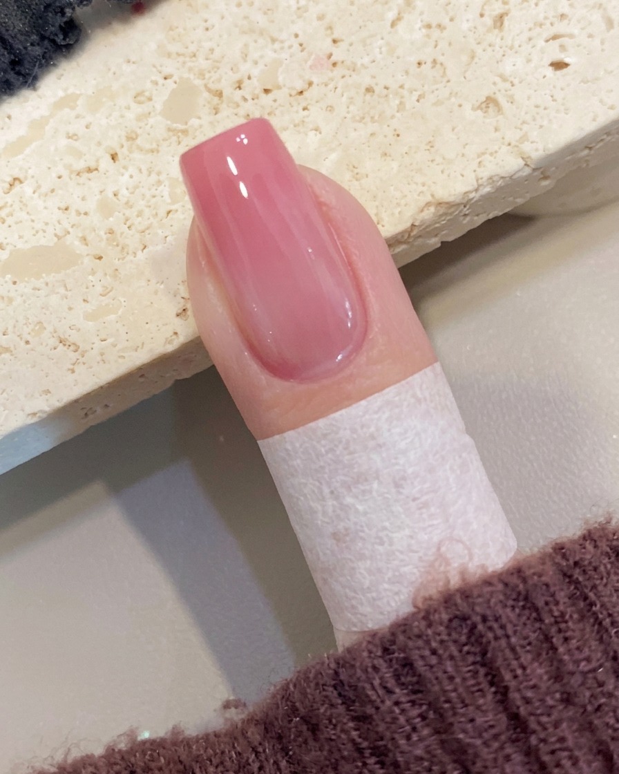 A brush applying a final layer of clear, high-gloss top coat to a peach ombre nail.