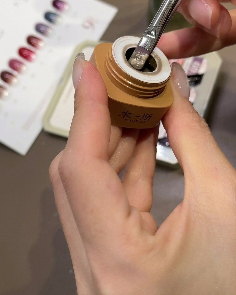 A brush applying beige peach cat-eye gel onto a clear nail tip.