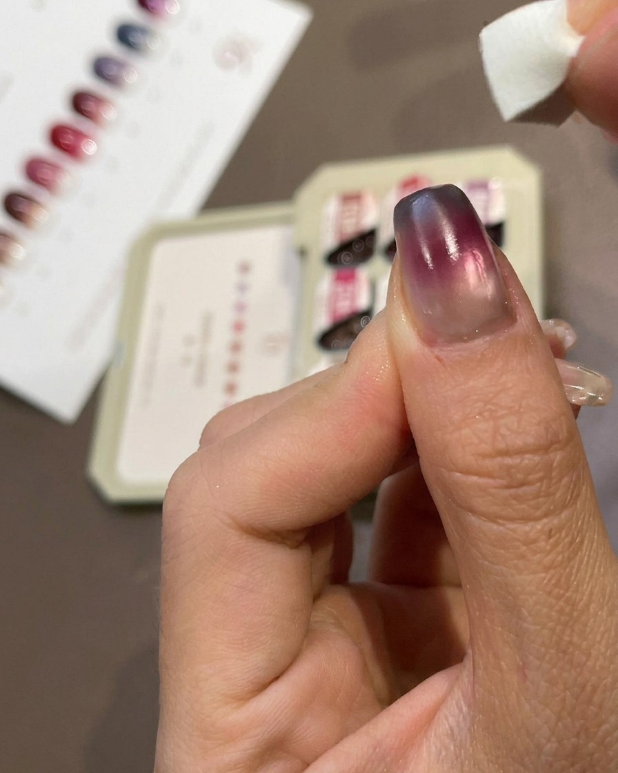 A close-up of a finger showing a small makeup sponge patting blue gel onto the very tip of a manicured nail.