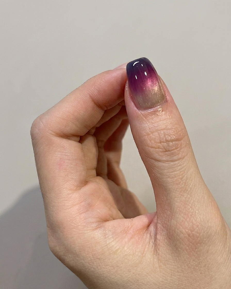 A brush applying a final, shiny top coat over a completed blue-purple ombre nail design.