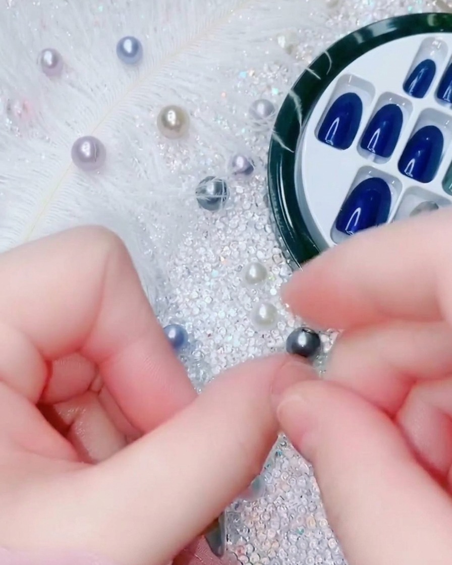 A close-up view of a finger pressing down on the center of an electric blue press-on nail to bond it to the nail bed.