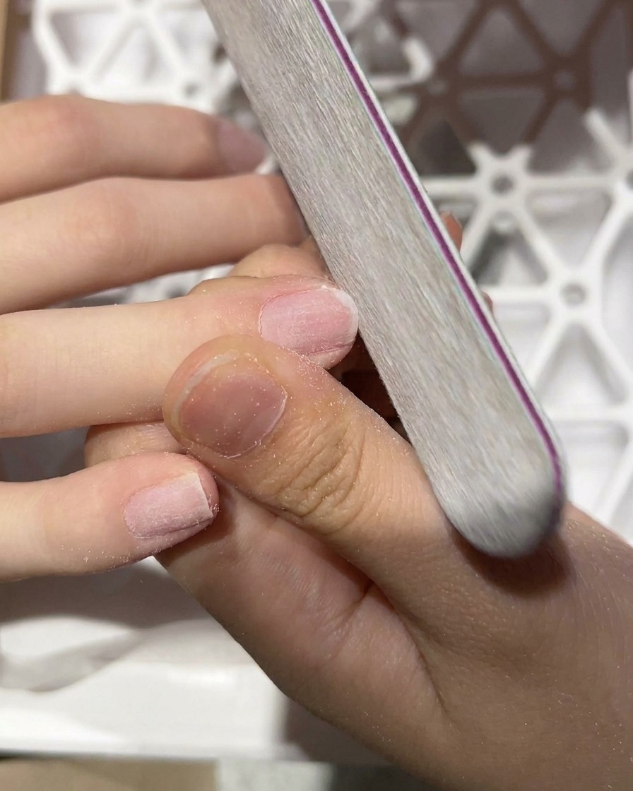 A close-up shot of a hand file buffing the surface of a natural nail.