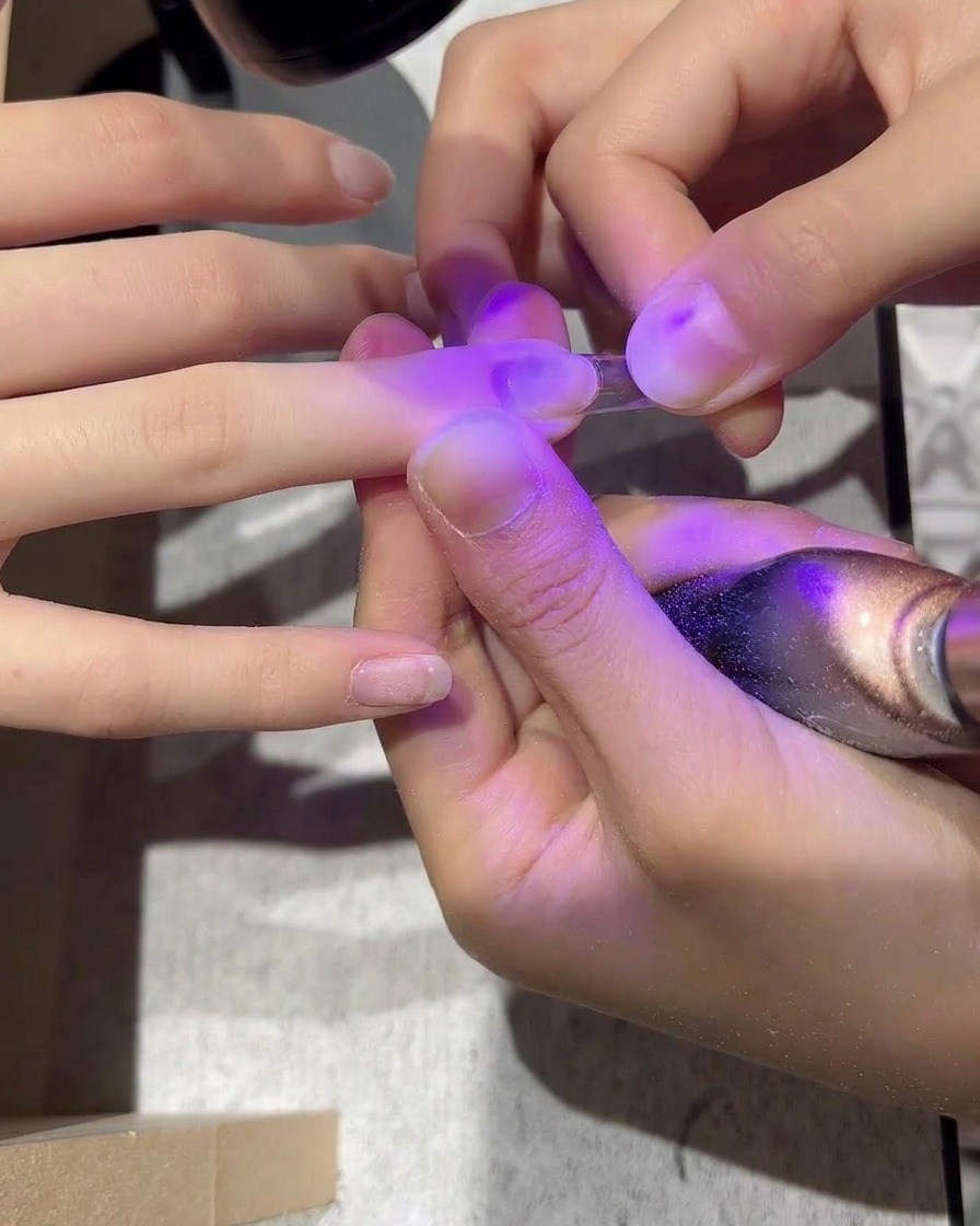 A clear plastic nail tip being applied to a natural nail with an adhesive.