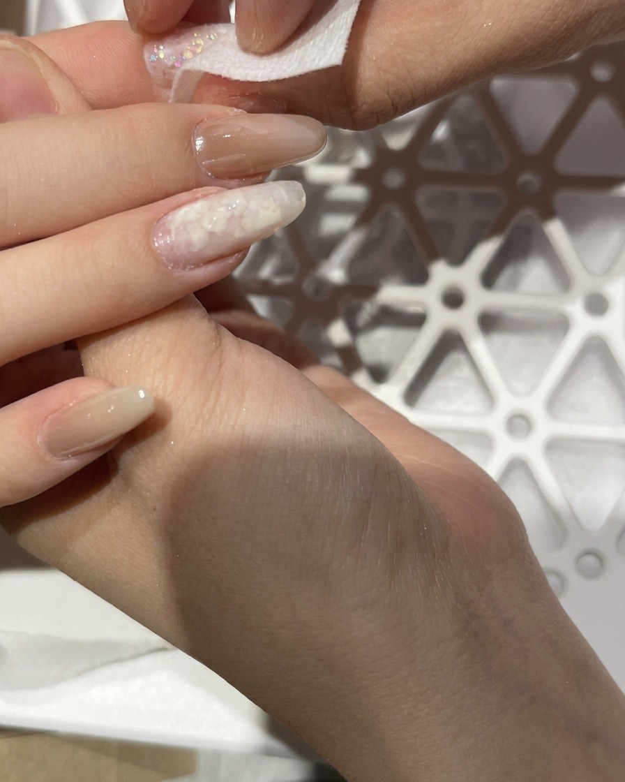 A hand using a lint-free wipe to clean off excess dust from a chrome-finished nail.