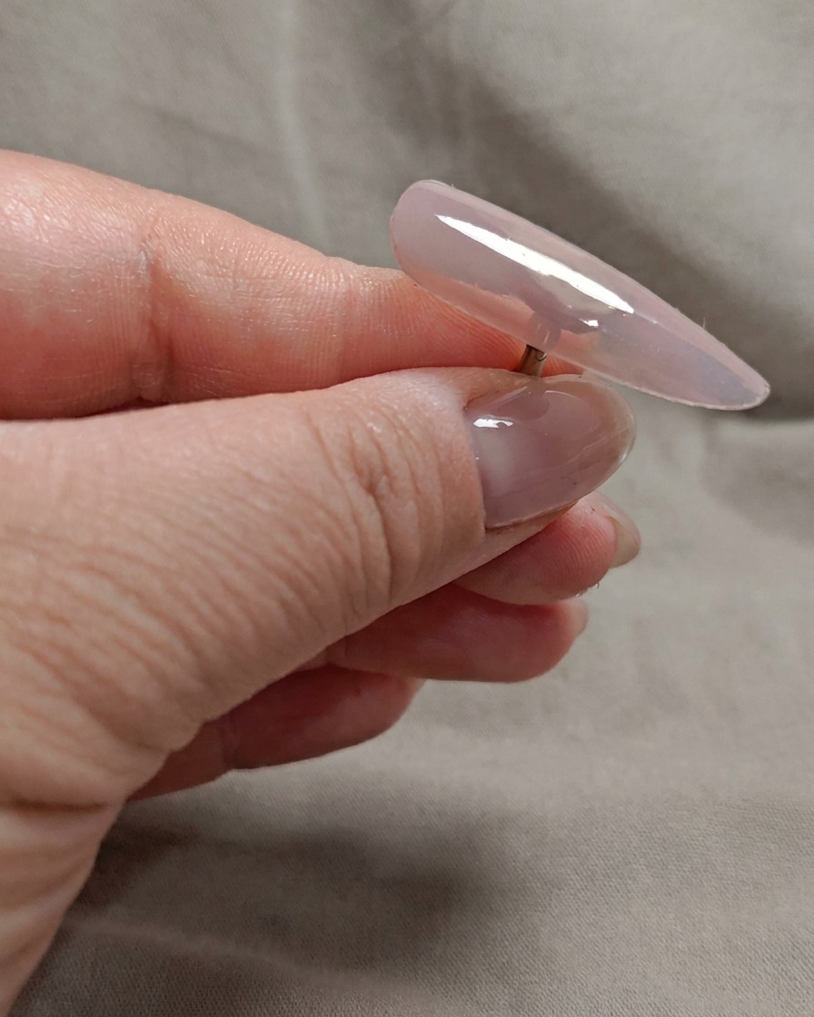 A brush applying a second layer of sheer nude pink gel to the nail tip.