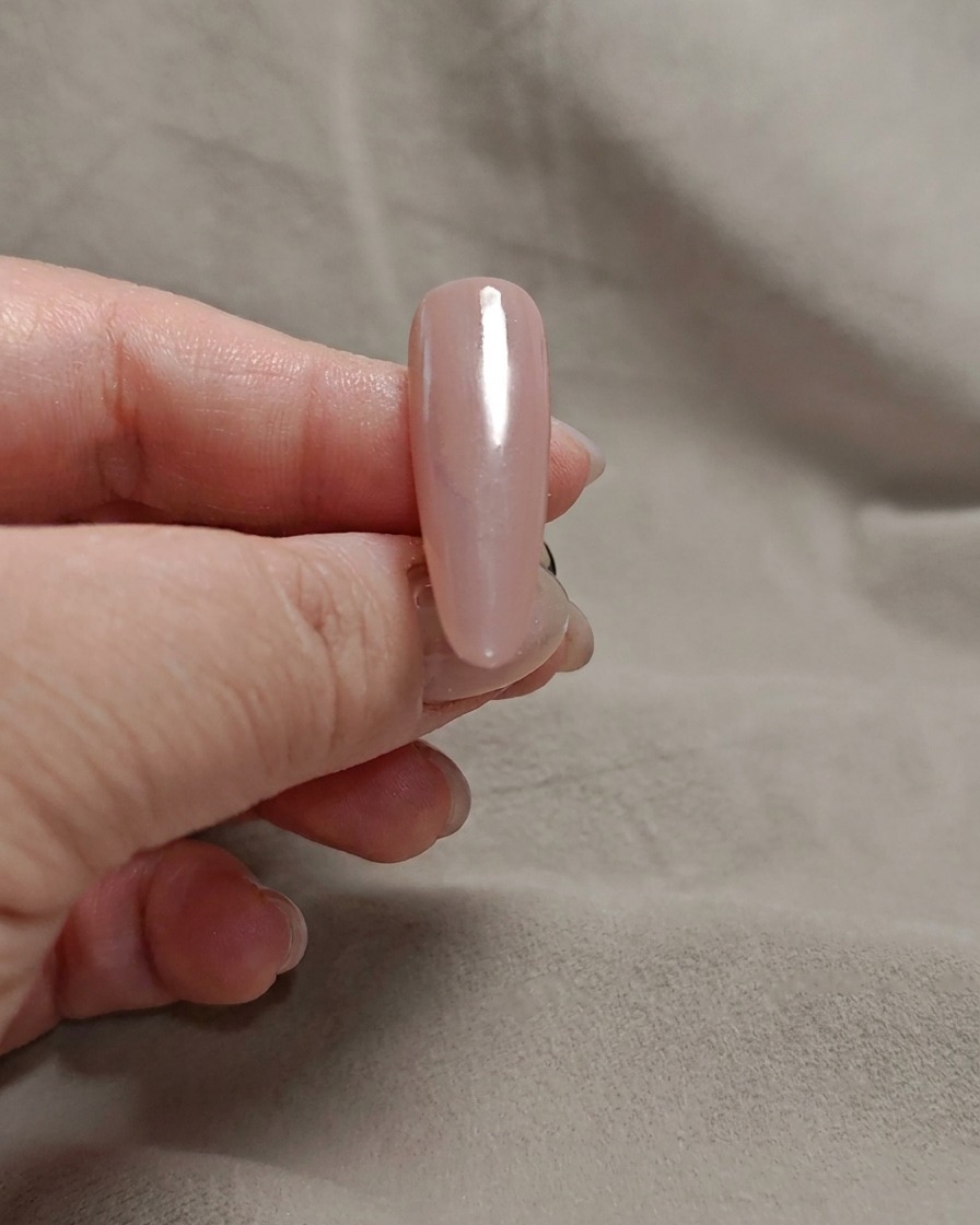 A makeup sponge dabbing milky white gel onto the tip of a pink nail.