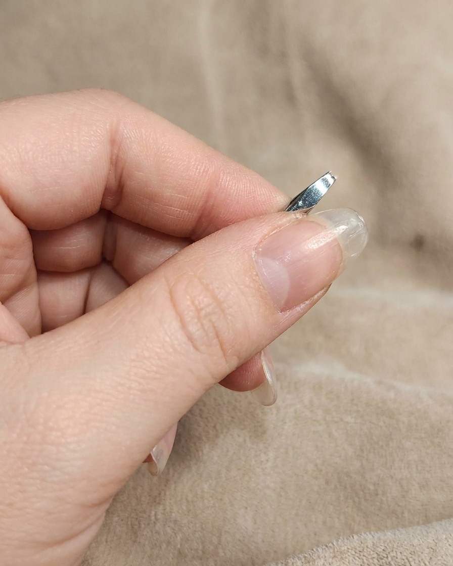 A close-up of a manicured nail being rubbed with white chrome powder using a finger.