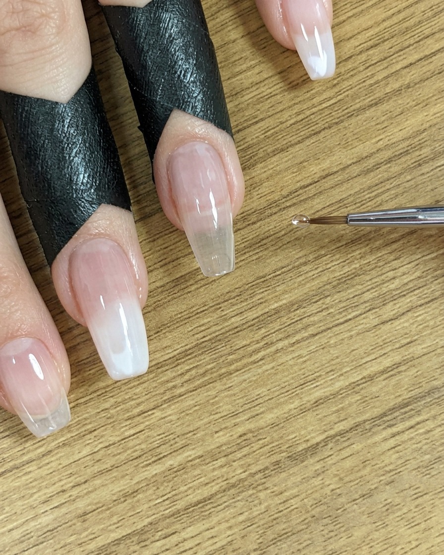 A small brush tip positioned near nails, ready for the next application step.