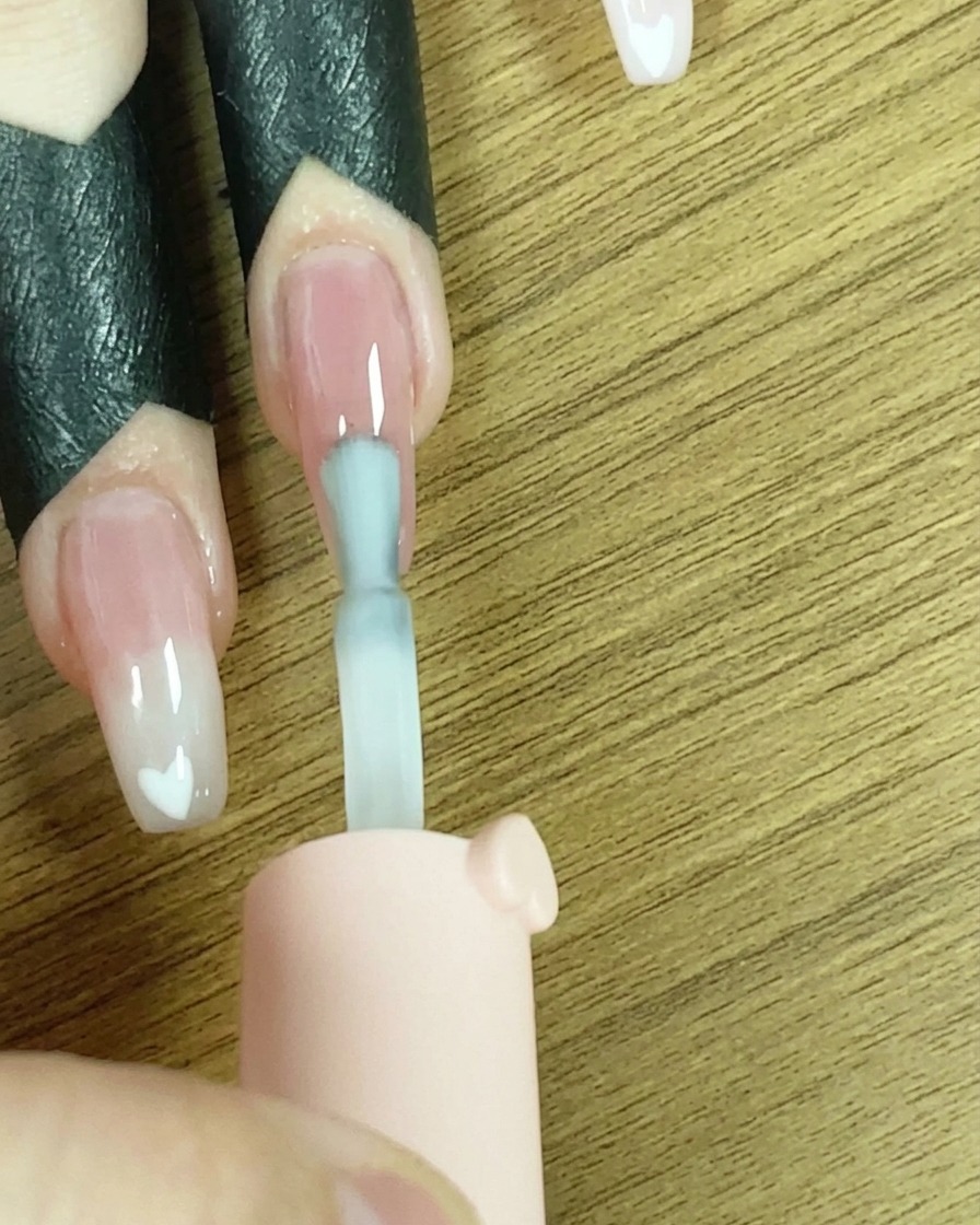 A brush applying a line of white gel polish across the tip of the nail.