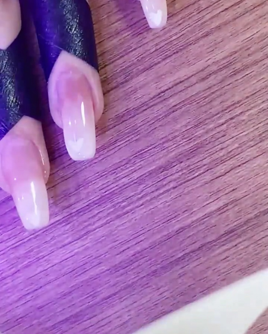 A hand curing the heart nail art design under a UV/LED lamp.
