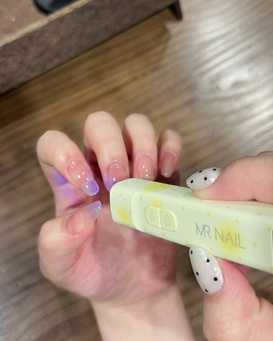 Nails positioned under a small, handheld MR NAIL branded UV lamp for curing.