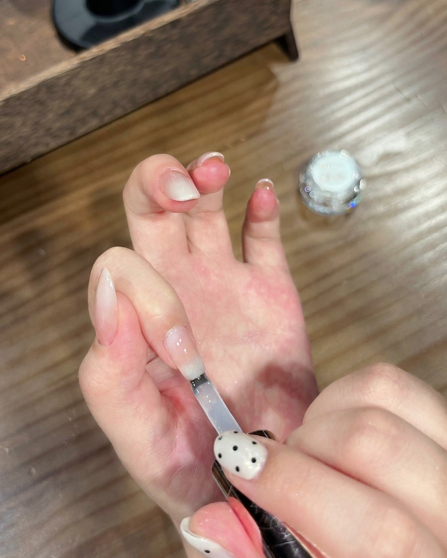 A brush applying a clear top coat to a finished chrome-effect gradient nail.