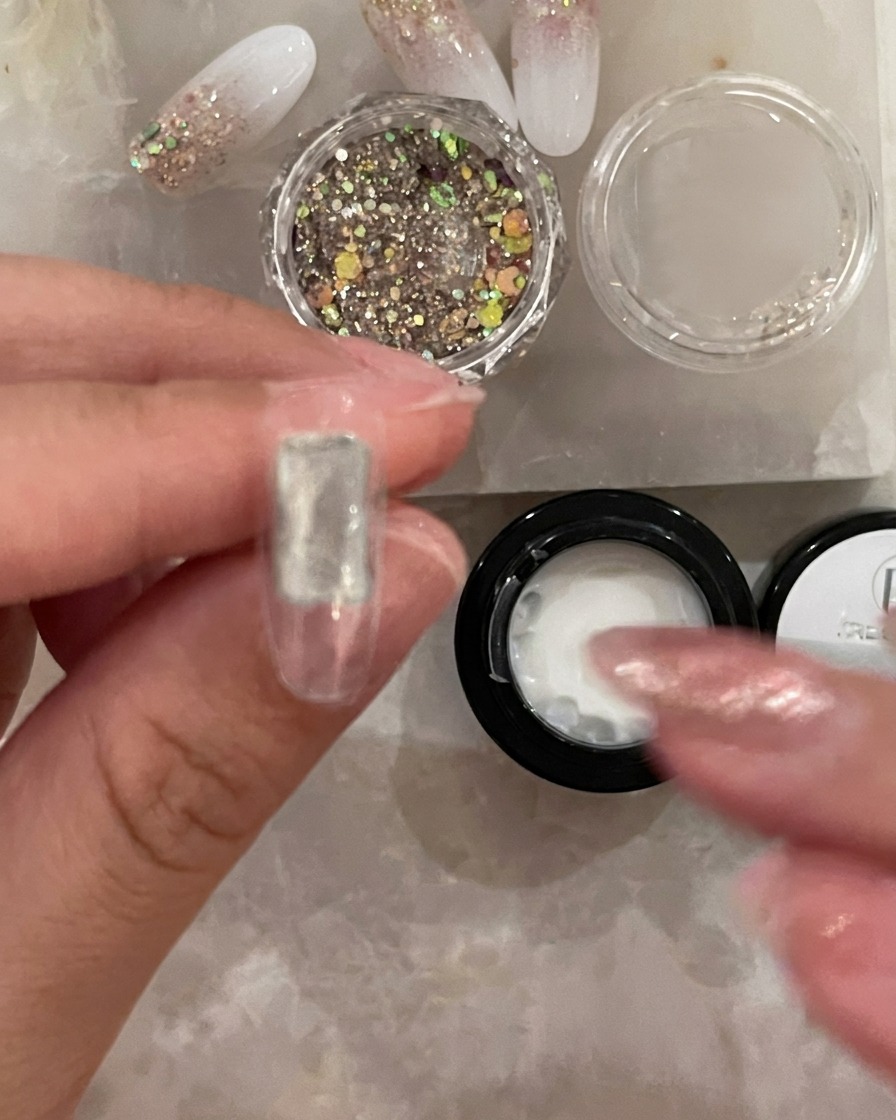 A small brush applying a clear, thin layer of base coat to the center of a clear artificial nail tip.