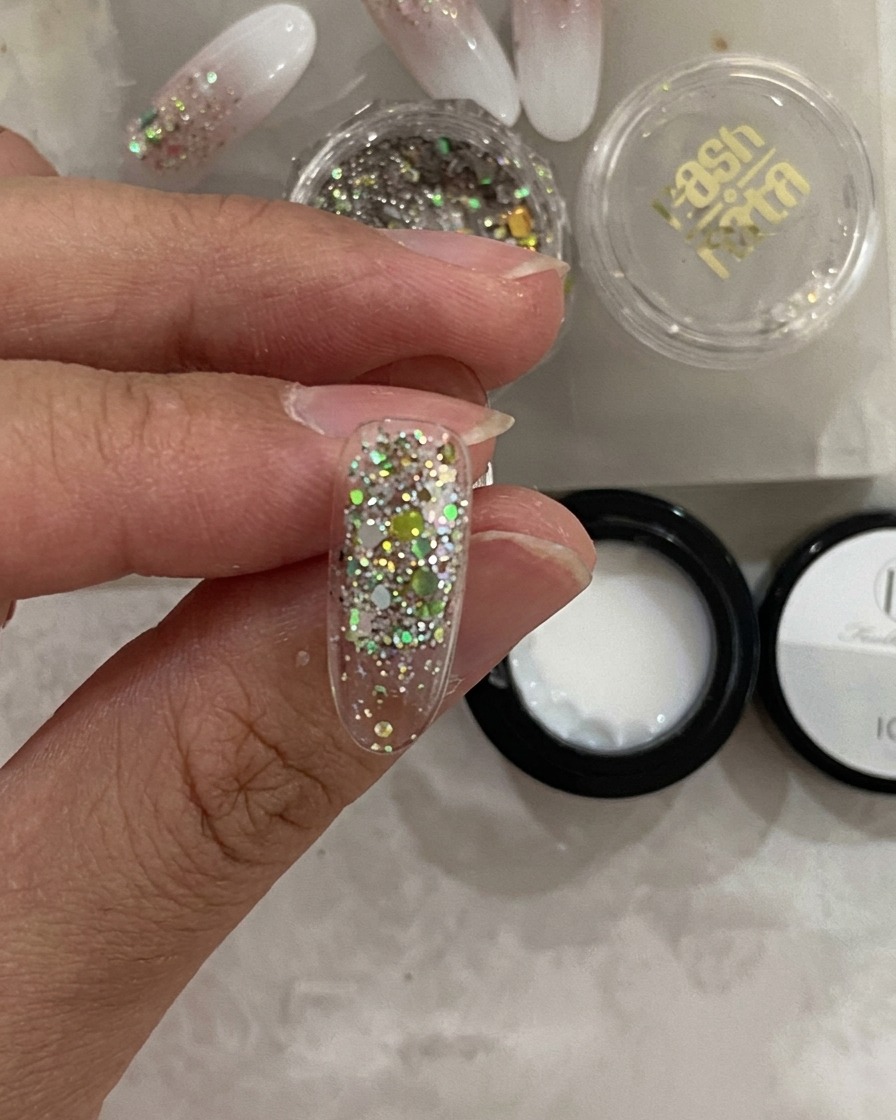 A close-up view of a nail tip inside a UV lamp, with the glitter layer appearing set.