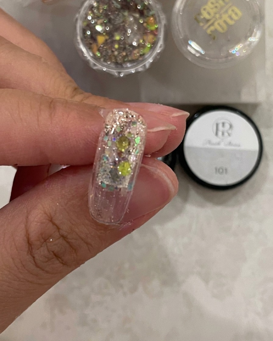 A close-up of a nail tip under curing light, showing the structure gel set over the glitter.