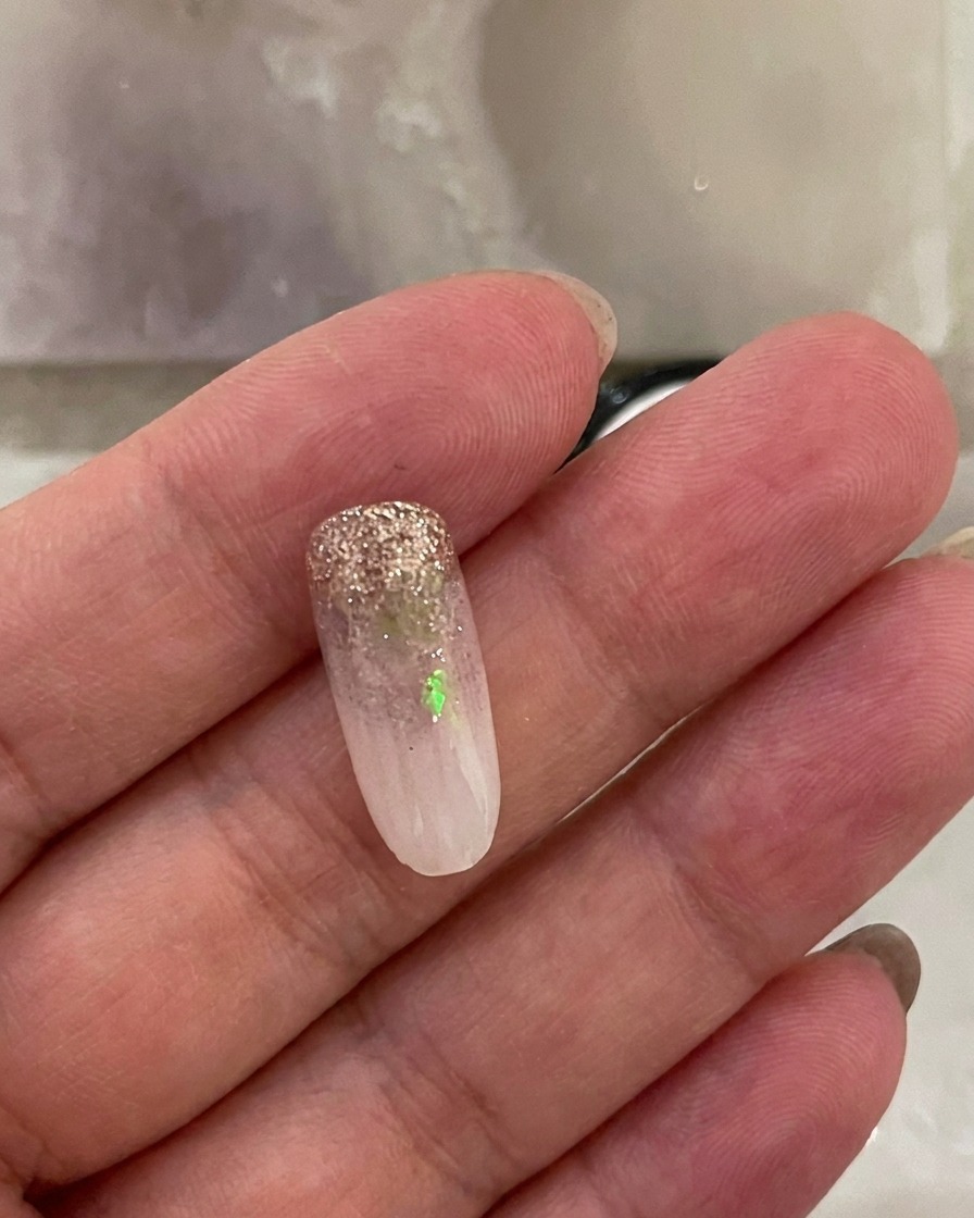 A fingernail with the milky white gradient applied, resting inside a UV nail lamp while the light is active.