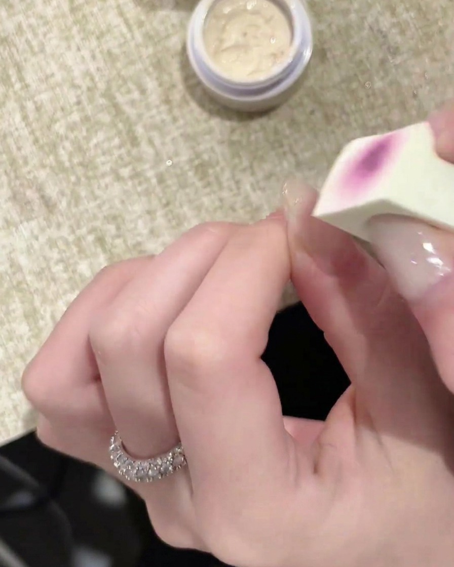 A close-up of a sponge tip applicator applying a layer of white gel to a fingernail.