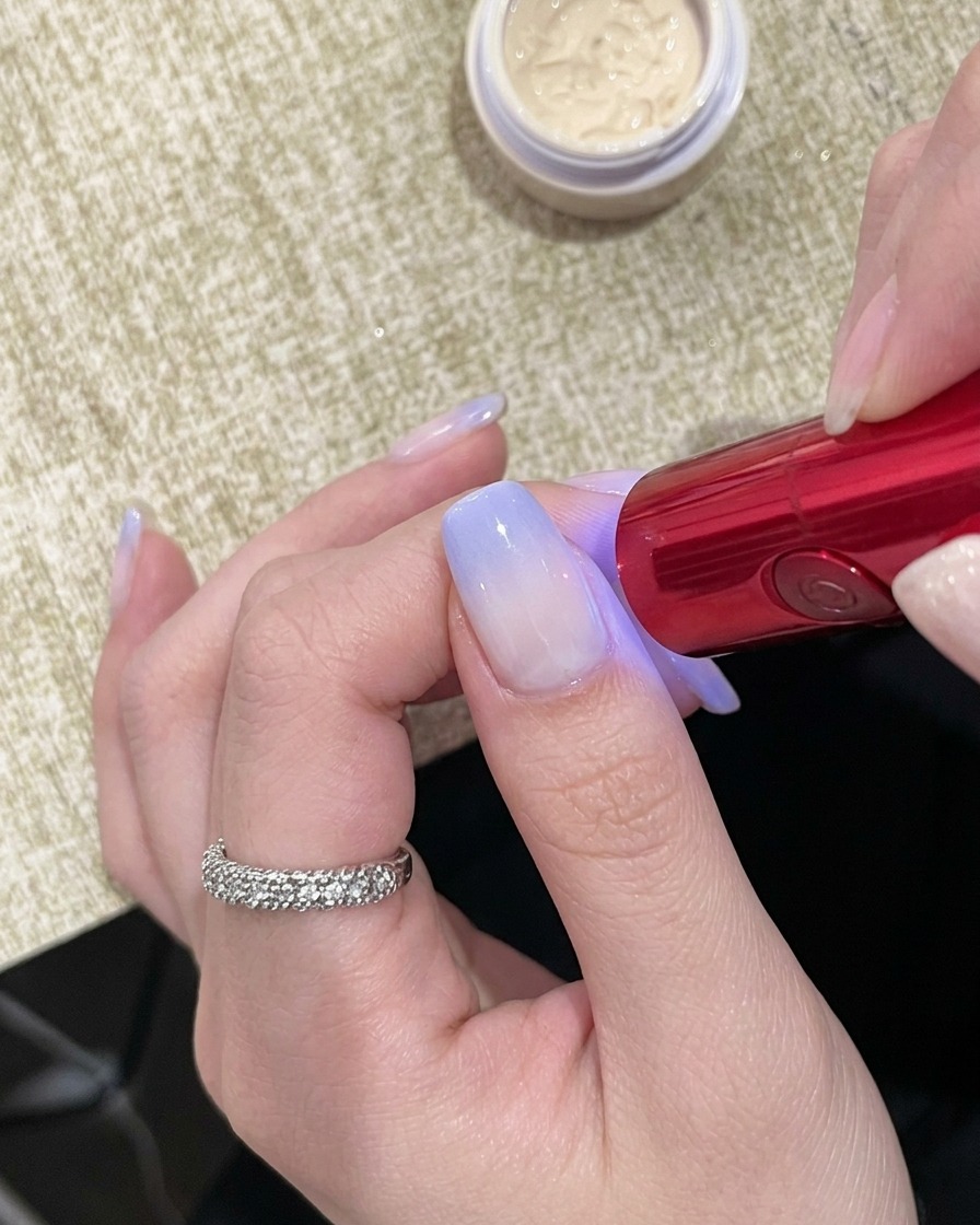 A hand positioned under a compact, handheld red UV lamp with the nails visible underneath.