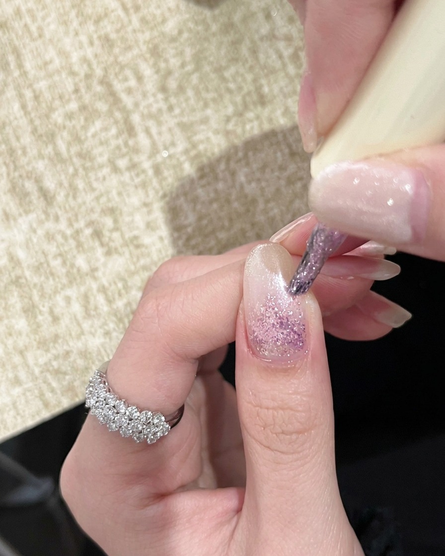 A hand under a handheld UV lamp with nails showing a light pink gradient effect.