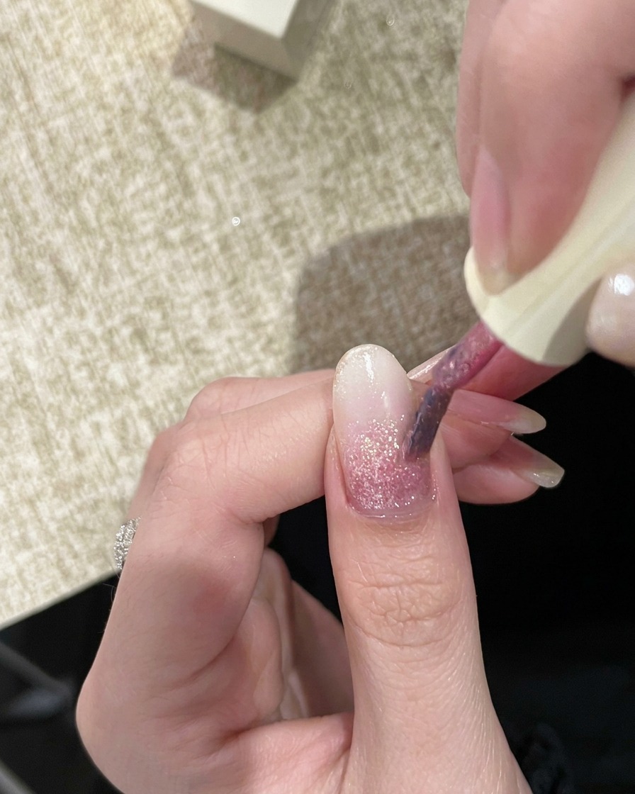 A nail brush applying a second, slightly more pigmented pink glitter gel to the nail.