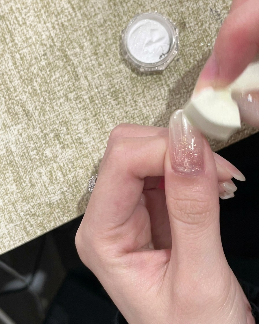 A sponge applicator dabbing gold chrome powder onto the free edge of a nail.
