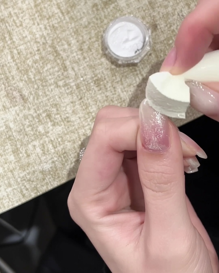 A brush applying a final glossy top coat over the gold chrome-tipped nail.