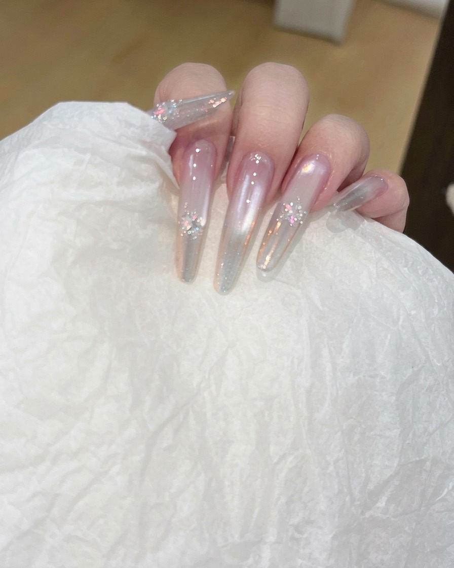 A close-up of a hand using a pad to clean the surface of a long, clear nail.