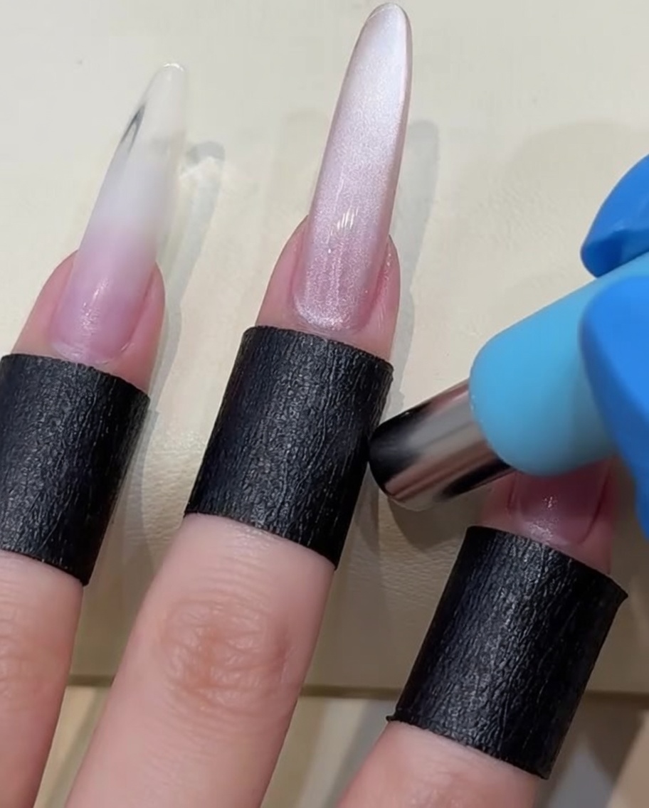 A cylindrical magnet being held close to a wet gel-painted nail to shift the magnetic particles.