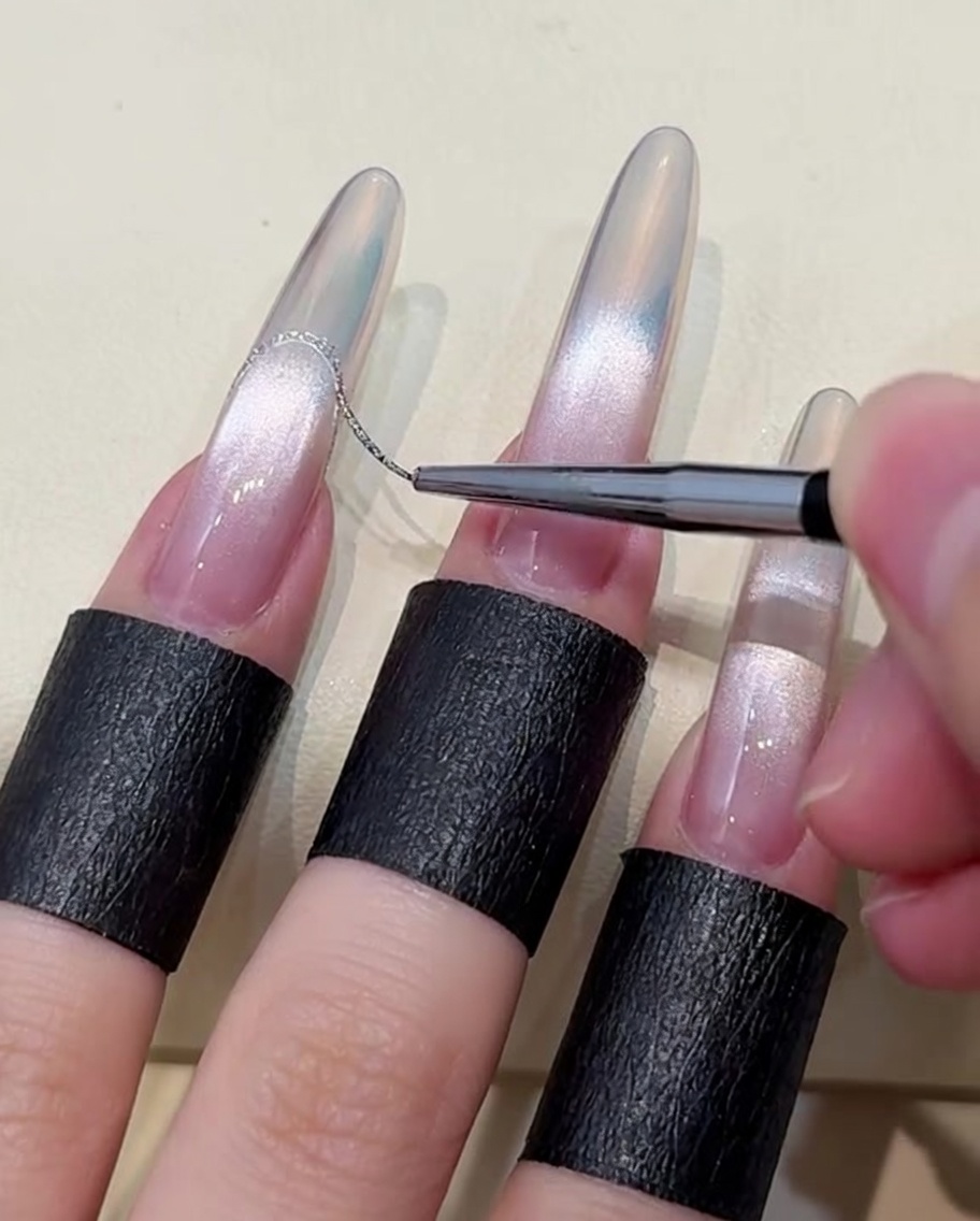 A close-up view of a fine liner brush applying a thin line of platinum silver gel to create a French tip on an aurora-gradient nail.