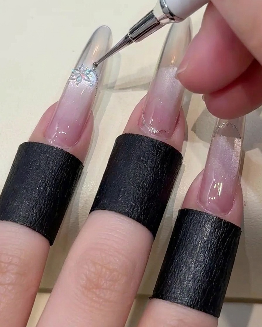 Close-up of tweezers placing a delicate snowflake-shaped crystal and tiny steel accent beads onto the nail.