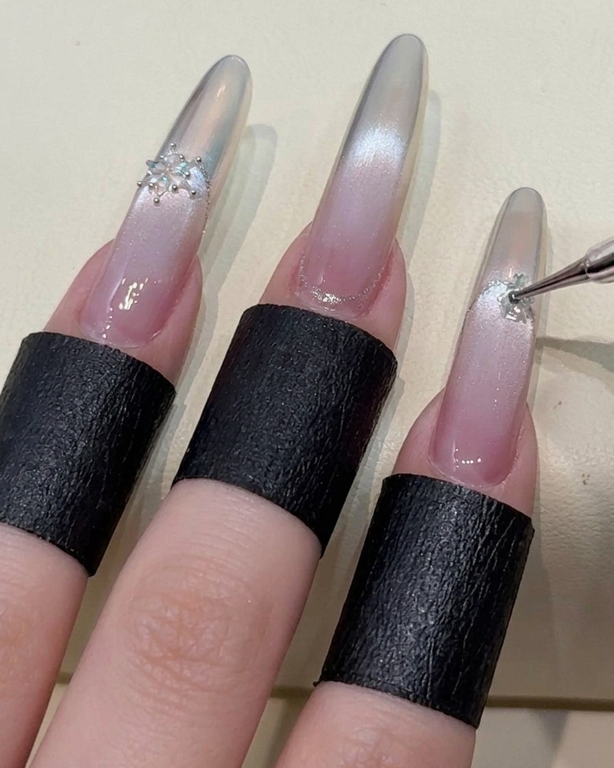 An index finger being decorated with a snowflake crystal accent, highlighting the detailed nail art process.