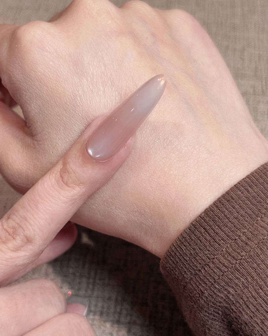 A close-up of a brush applying a thin, smooth layer of nude gel polish onto a prepped nail.
