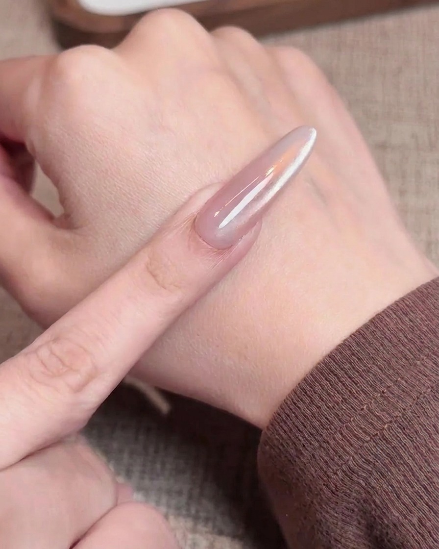 An eyeshadow applicator buffing iridescent aurora chrome powder onto the tip of a nail, creating a gradient effect.