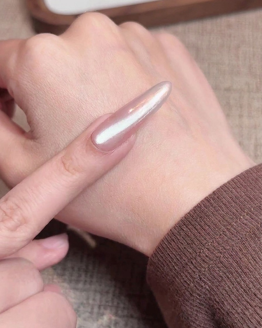 A brush applying a coat of shimmery cat eye gel over a nail with a chrome gradient finish.