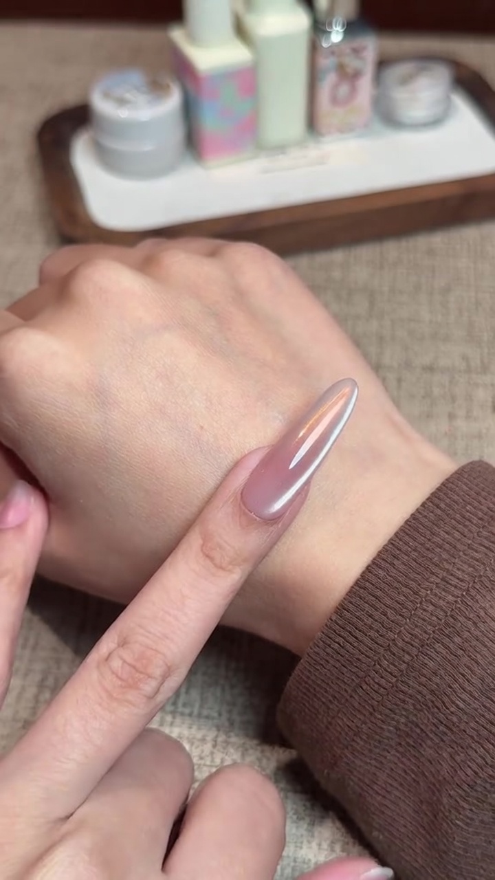 Close-up of a long, almond-shaped nail featuring a smooth, iridescent aurora chrome finish over a soft pink gradient base, with a subtle side cat-eye magnetic reflection.