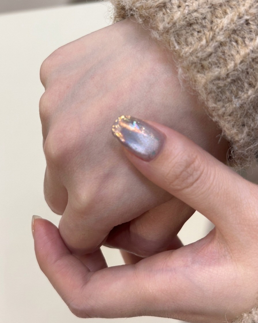 A brush applying a coat of silver cat-eye gel polish onto a natural fingernail.