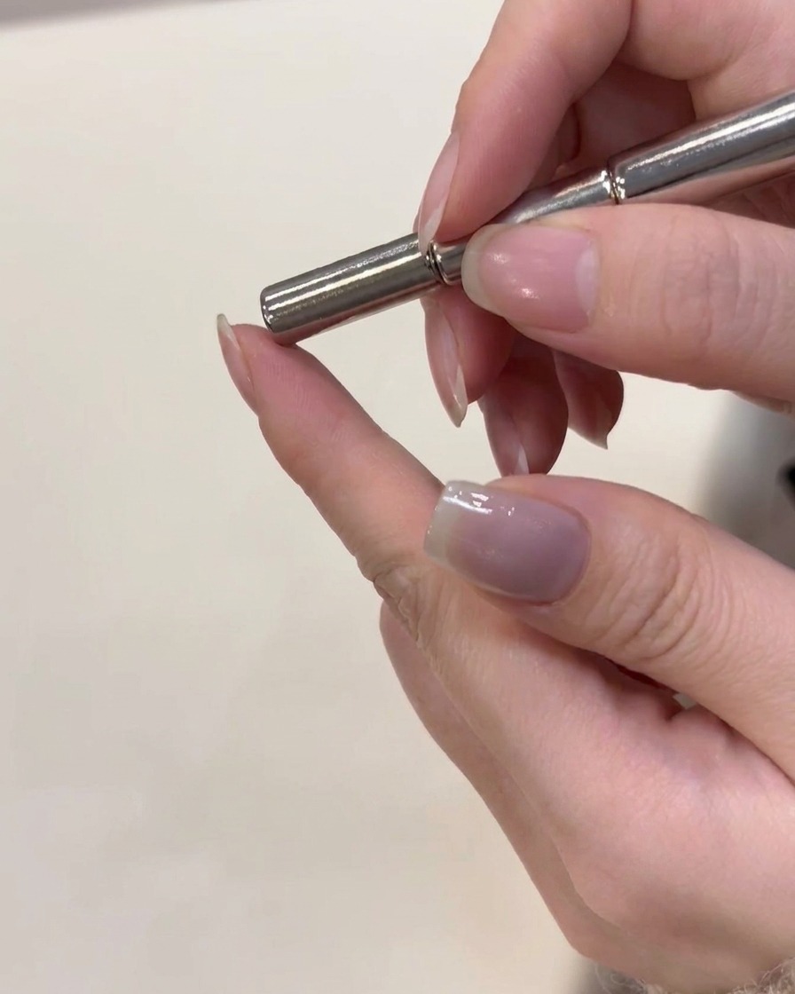 A magnetic tool being held just above a freshly coated silver cat-eye gel nail to shape the magnetic particles.