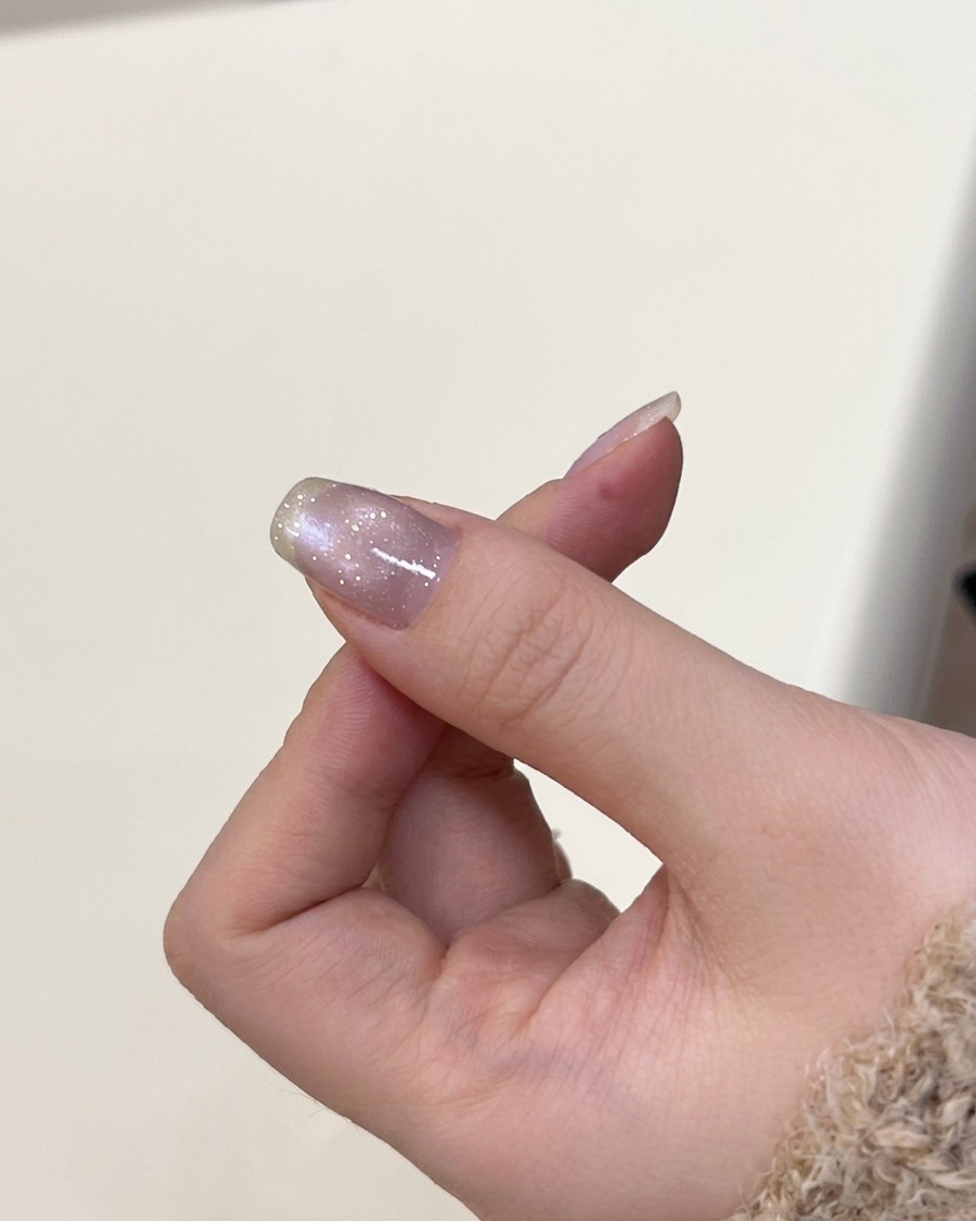 A hand positioned inside a UV nail lamp to cure the recently applied cat-eye gel.