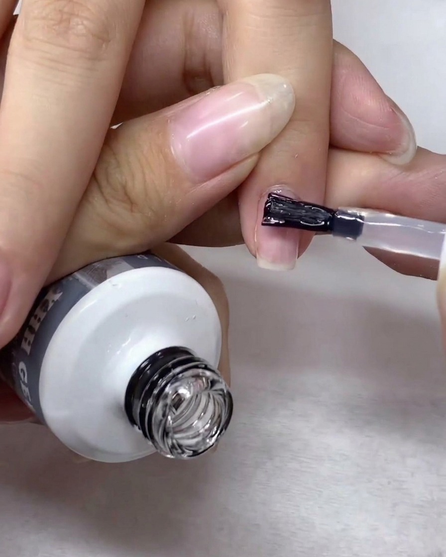 A nail art brush gently spreading and smoothing clear strengthening gel across the entire surface of the nail.
