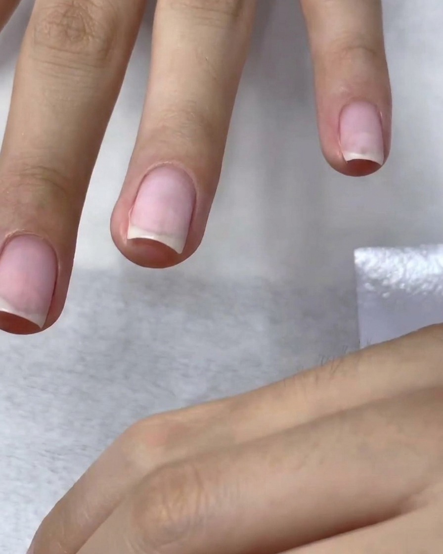 A buffing block lightly sanding the surface of a nail to create a smooth, matte finish for color application.